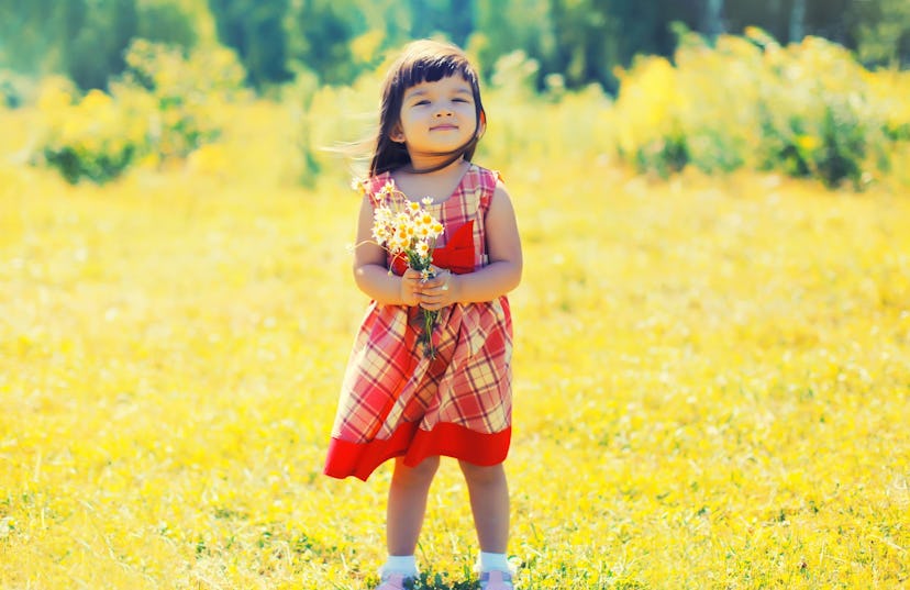 Happy smiling little girl child outdoors with bouquet of wildflowers walking in sunny summer park