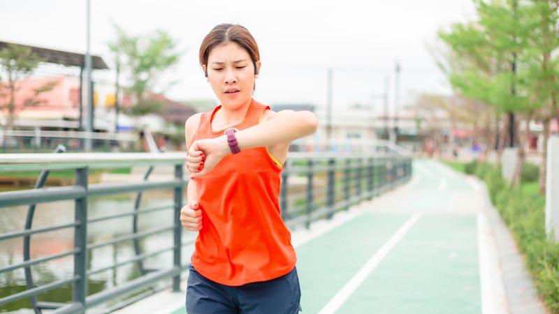 Asian athletic woman running and looking at sport watch. Young female runner jogging during outdoor ...