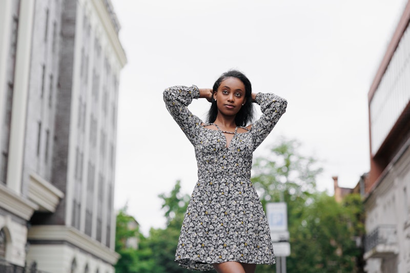 Young african pensive woman in summer dress walks in city against background of building. Bottom vie...