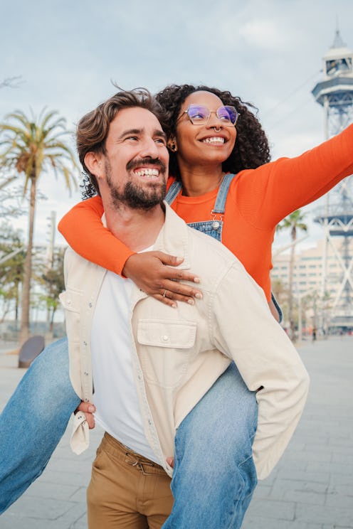 Vertical portrait of couple having fun together on a romantic date. Smiling man giving a piggyback r...