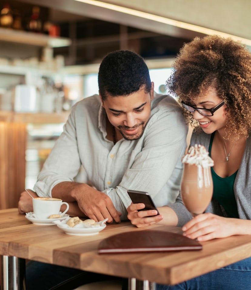 Young couple using a smart phone in a cafe while enjoying a cup of coffee