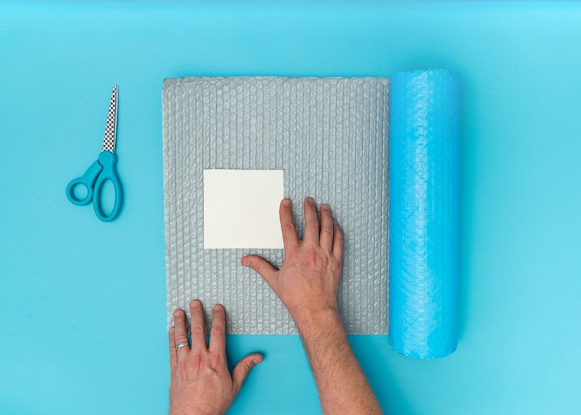 Caucasian adult male hands packaging blank white square paper with bubblewrap and scissors