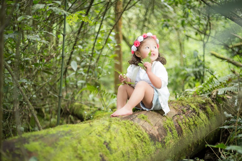 Girl sitting on a trunk in the middle of a big green forest smelling the happy and quiet herb
