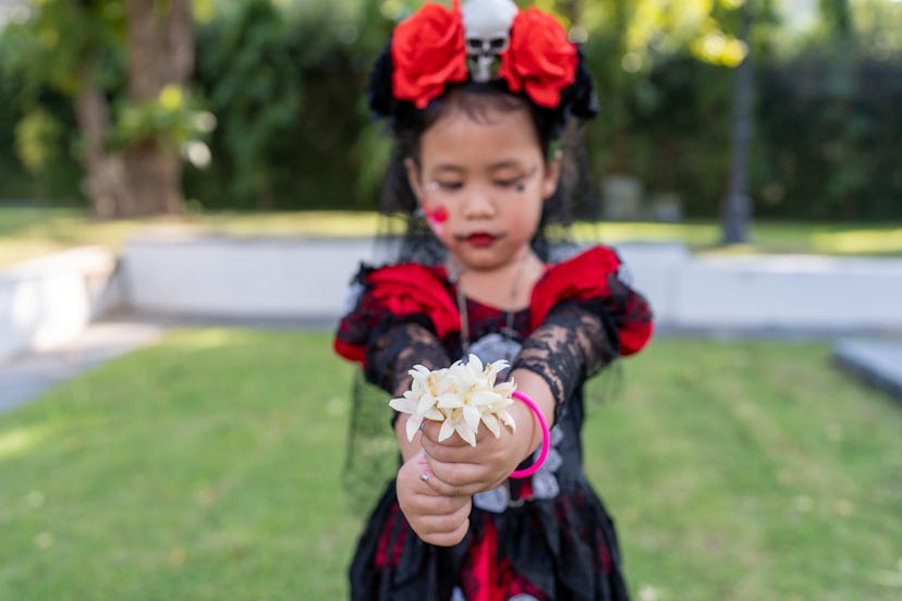 Small girl in red dressed holding white flower at garden.