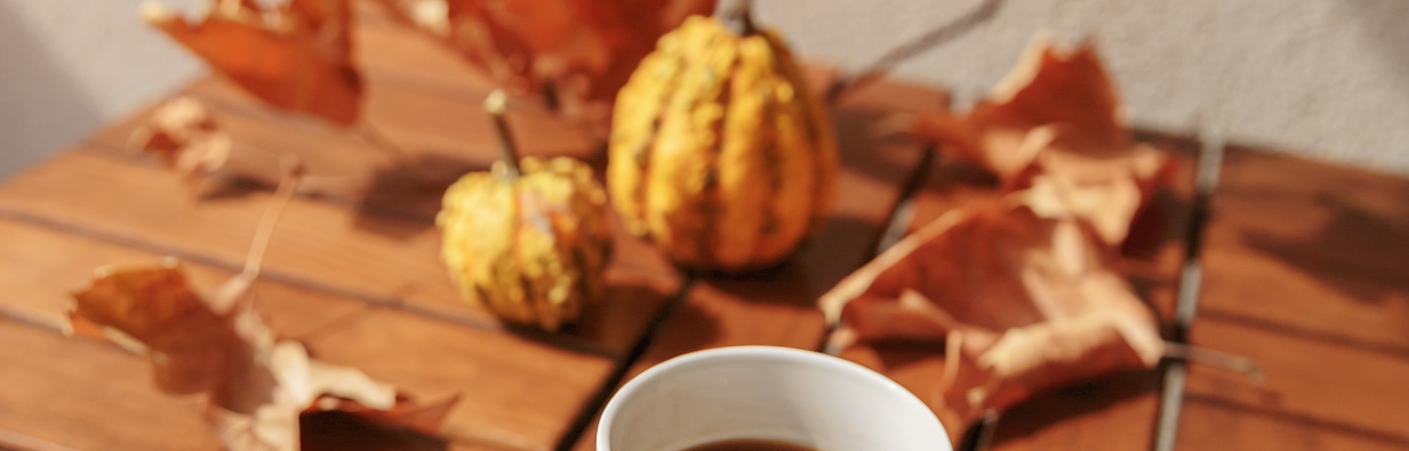 Morning cup of coffee on wooden table decorated with pumpkins and dried flowers outdoor. A woman's h...