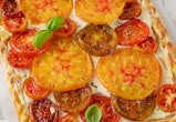 Tomatoes pie or galette from puff pastry and cheese filling on a white wooden background. Vegetarian...