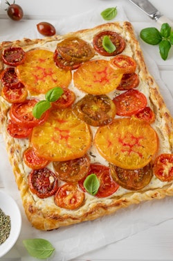 Tomatoes pie or galette from puff pastry and cheese filling on a white wooden background. Vegetarian...
