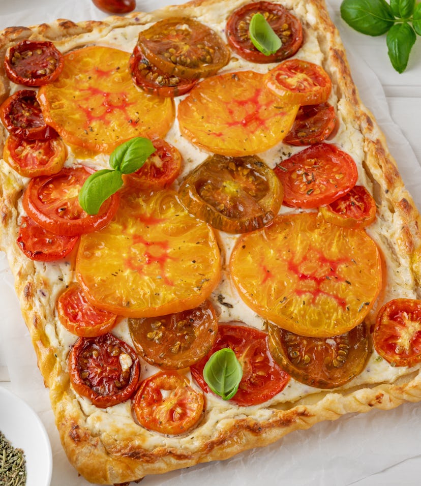 Tomatoes pie or galette from puff pastry and cheese filling on a white wooden background. Vegetarian...