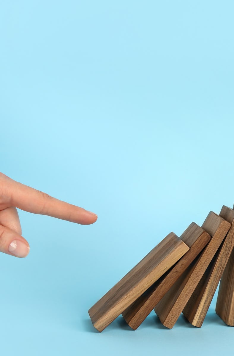 Woman causing chain reaction by pushing domino tile on light blue background, closeup