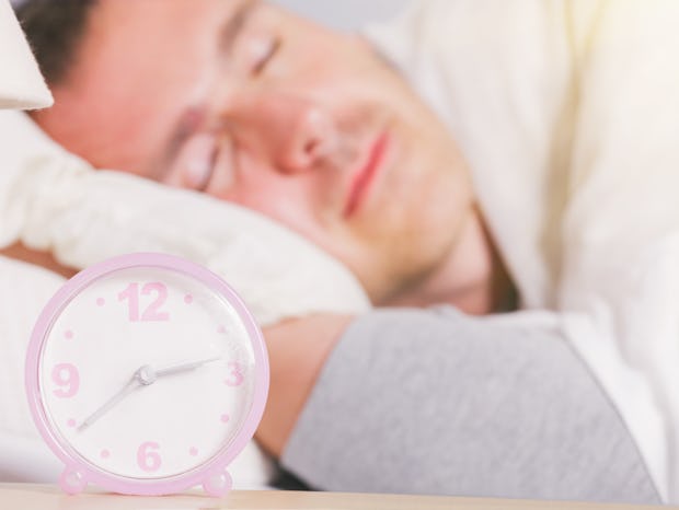 Man is sleeping at home. The alarm clock visible in the foreground 