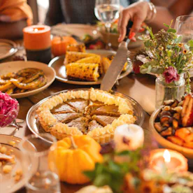 Festive table with Thanksgiving dishes, including pie, corn, and vegetables. People enjoying a meal,...