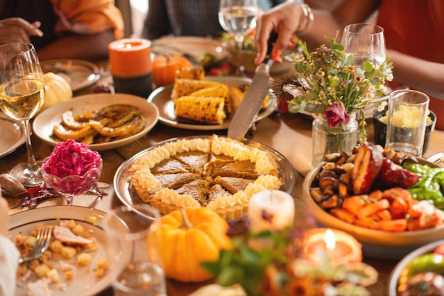 Festive table with Thanksgiving dishes, including pie, corn, and vegetables. People enjoying a meal,...
