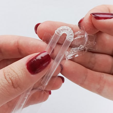 Women's hands open the packaging of a disposable juice tube.A plastic juice straw in close-up in you...