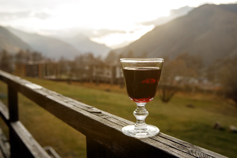 A glass of red liquor against the backdrop of a mountain valley