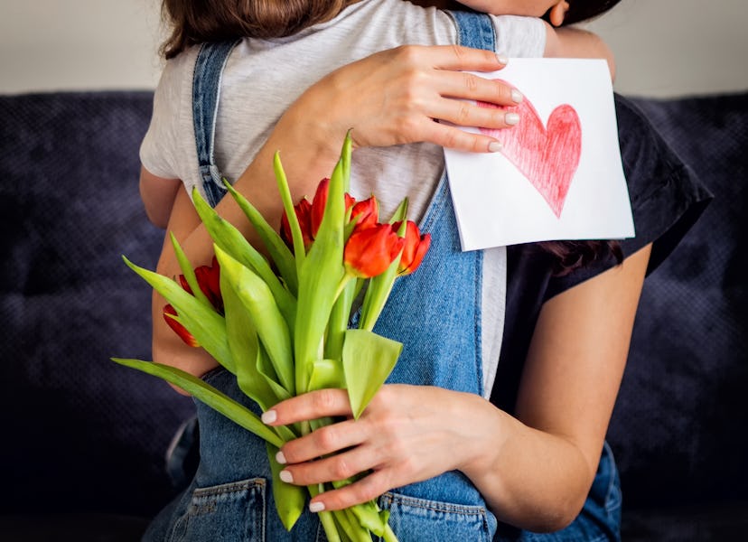 Tender moment as a young girl hugs her mom, presenting tulips and a handmade heart card