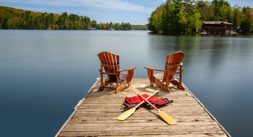 Two Adirondack chairs on a wooden dock face the serene blue waters of a Muskoka's lake. Canoe paddle...