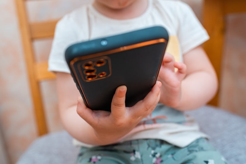 Un bébé, un tout-petit, un nourrisson, un enfant de 1,2 ans assis et utilisant un téléphone portable, la technologie à la maison. S'amuser...