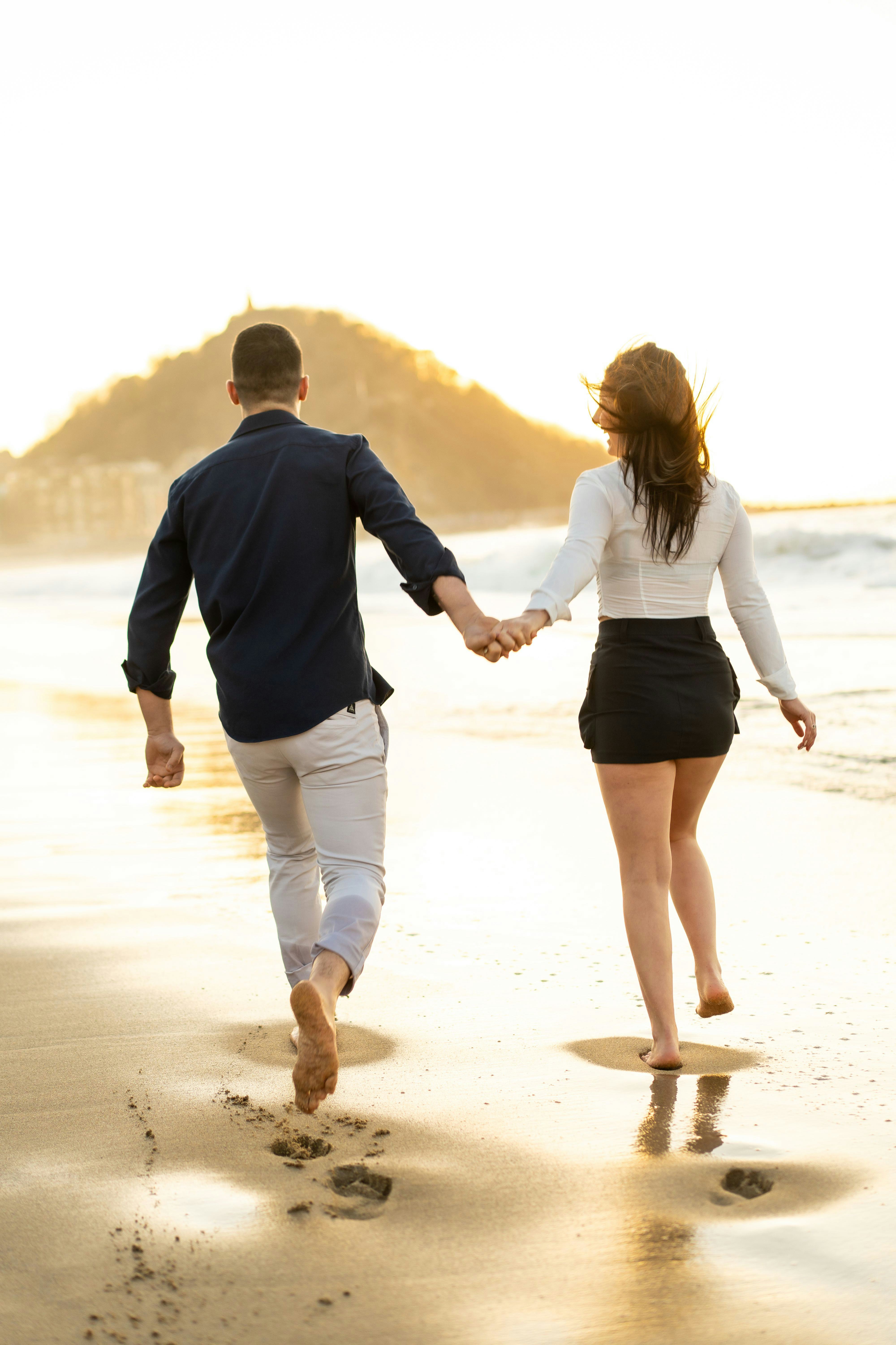 happy couple holding hands running along a beach during sunset