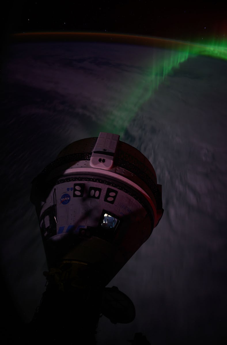 In this file photo, an aurora streams below Boeing's Starliner spacecraft docked to the forward port...
