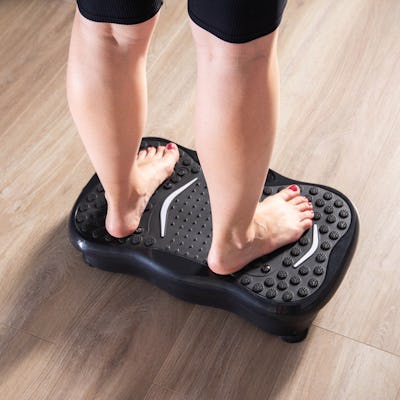Women's legs stand on a sports vibration platform at home. Concept of doing sports at home. Modern home exercise machine