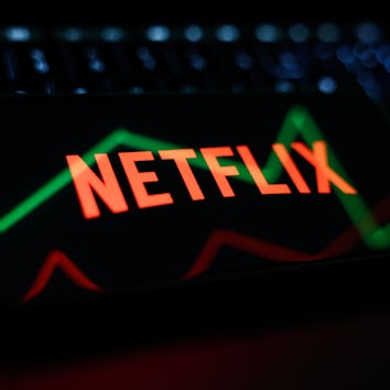 A laptop keyboard, a reflected illustrative stock graph displayed on a screen and Netflix logo disla...