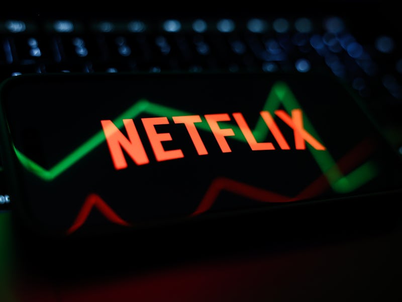 A laptop keyboard, a reflected illustrative stock graph displayed on a screen and Netflix logo disla...