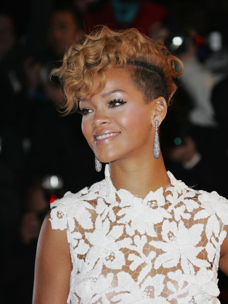 Rihanna in a white floral dress, sporting a curly blonde pompadour with shaved sides and a frosty wh...