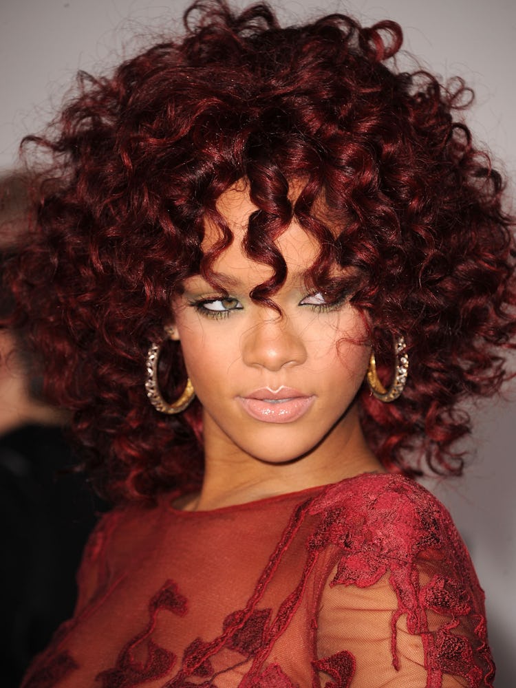 Rihanna with cherry red curly hair and large golden hoop earrings with a red dress at the 2010 AMA's...