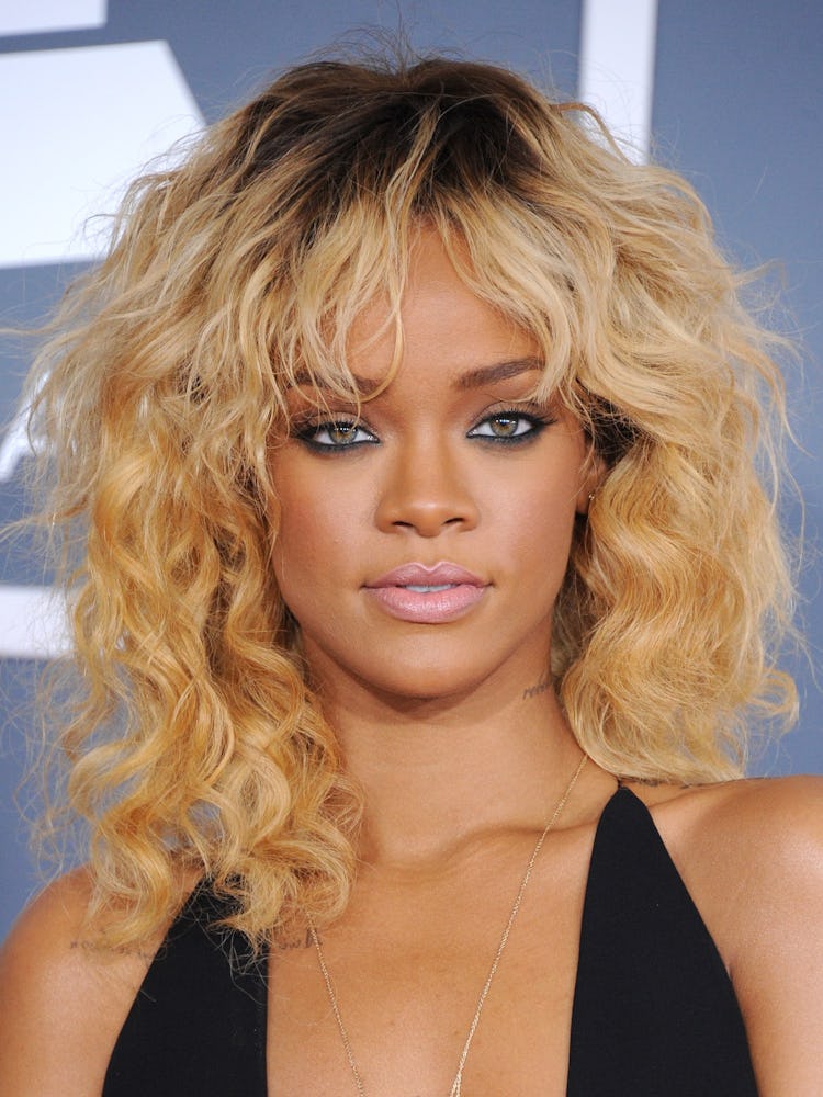 Rihanna with her hair in blonde beach waves and her dark roots slightly showing, wearing a black dre...