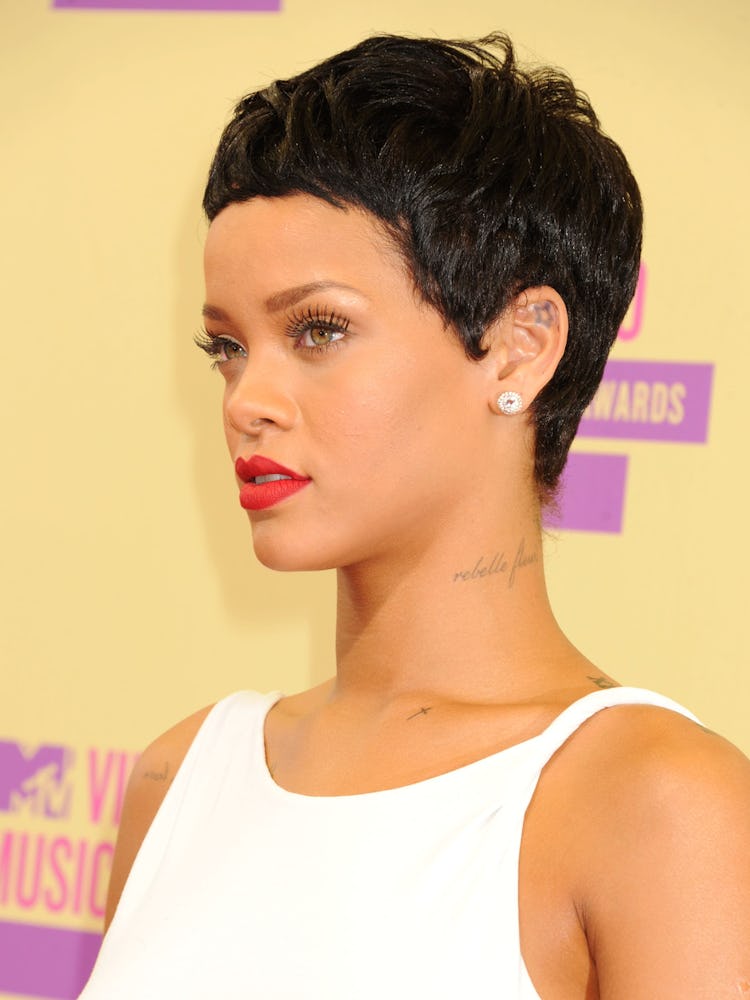 Rihanna looking to the side in a white dress and sporting a short pixie haircut with red lipstick at...