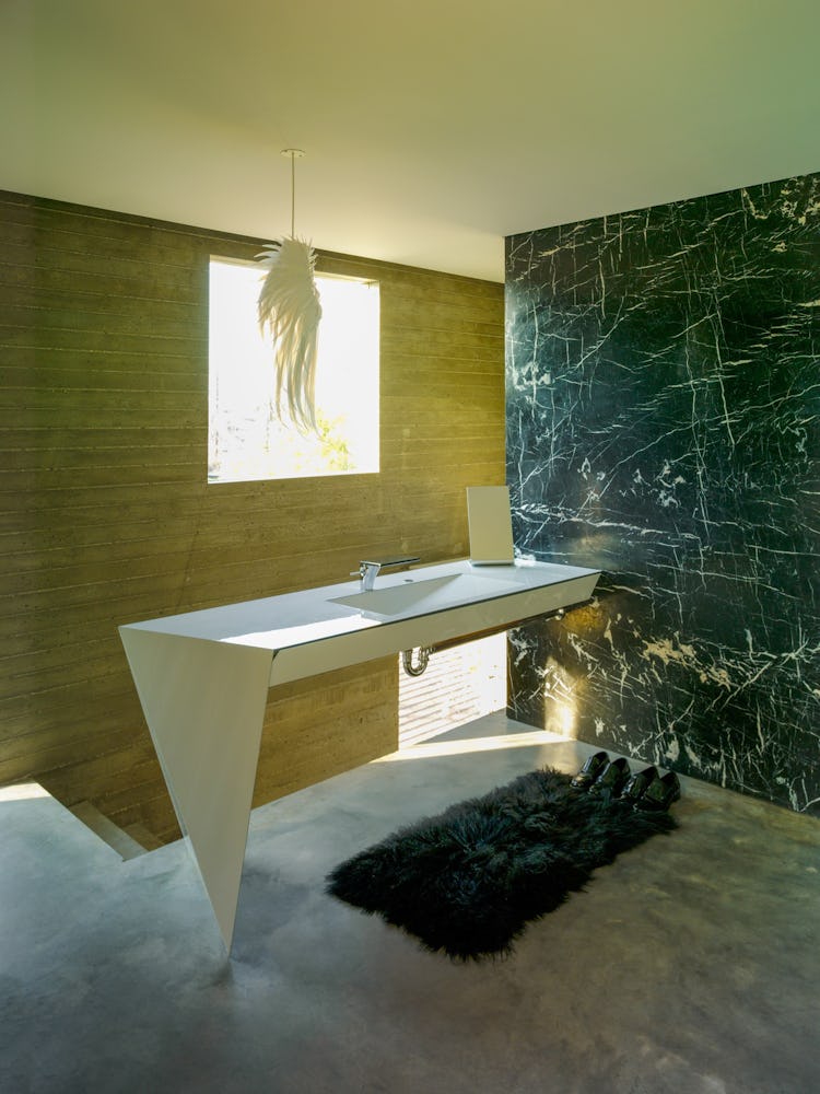 A white bathroom sink that connects to a dark green marble wall 