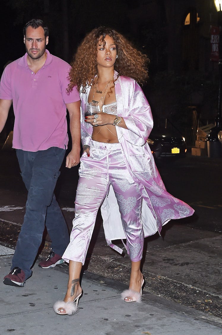 Rihanna walking while wearing a silk purple bra, pants, and coat combination