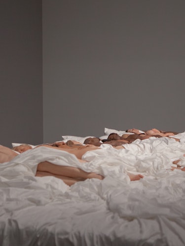 Doll bodies placed on a bed with white sheets as a part of Kanye West's Famous sculpture