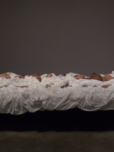 A full view of Kanye West's Famous sculpture with all the doll bodies laid out on a bed with white b...