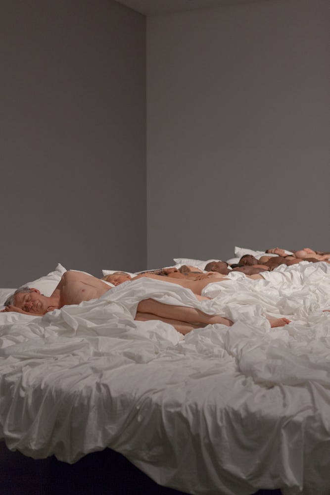 Installation view of Kanye West’s Famous sculpture with doll bodies lying in a bed with white sheets