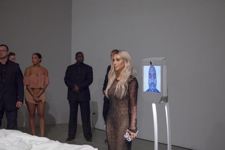 Kim Kardashian standing next to a small tv monitor with Kanye West visible on it in the gallery
