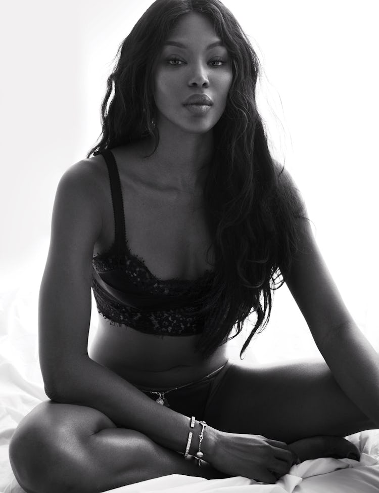 Naomi Campbell sitting in a black bralette