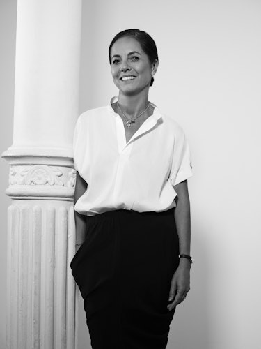 A woman standing and smiling in a white blouse and black trousers
