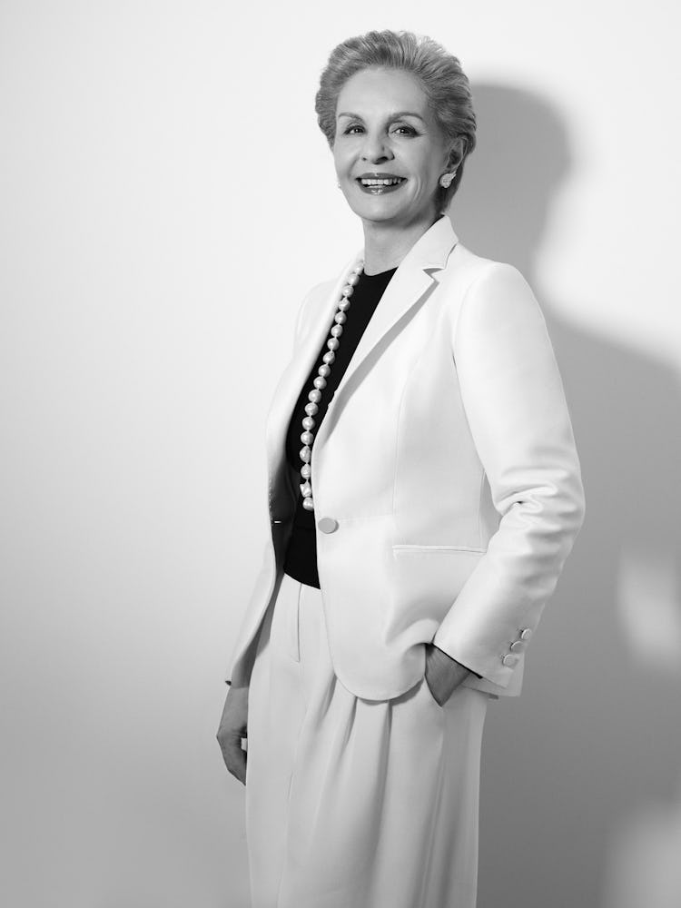 A woman in a white blazer and skirt, black shirt and a large necklace