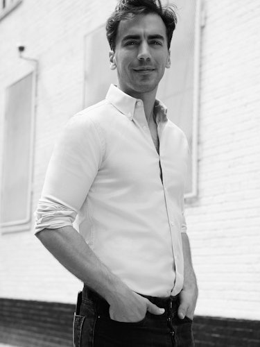 A man in a white shirt and black pants with his hands in his pocket standing and smiling