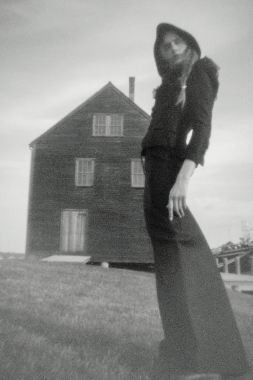 A model in a black dress with a hoodie in front of a house with a grainy black-white color filter
