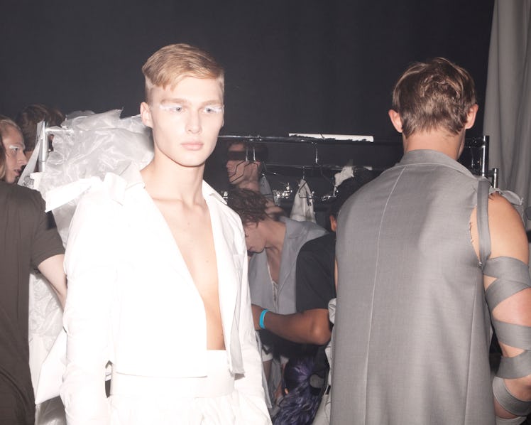 A male model in a white unbuttoned shirt and white pants backstage at VFiles' Spring 2017 show 