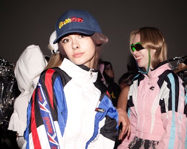 A model in a cap posing for the camera as other models are speaking behind her 