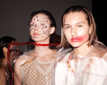 A model with her face painted in tattoos and the other with red lipstick smudged on her face waiting...