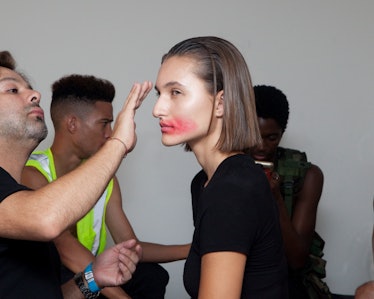A model in hair and makeup with red lipstick smudged on her face and lips backstage at the show 