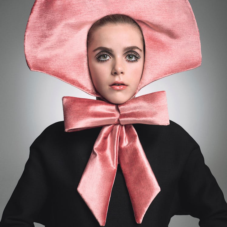 A female model posing while wearing a black Valentino dress and pink Franc Fernandez bonnet
