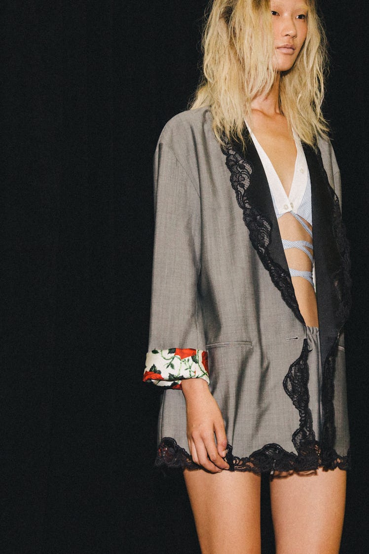 A model in a white bralette, shorts, and matching grey blazer with lace and flower print details at ...