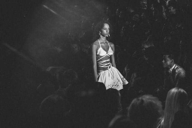 A model in a white leather skirt and strappy bralette walking the runway during Alexander Wang Sprin...