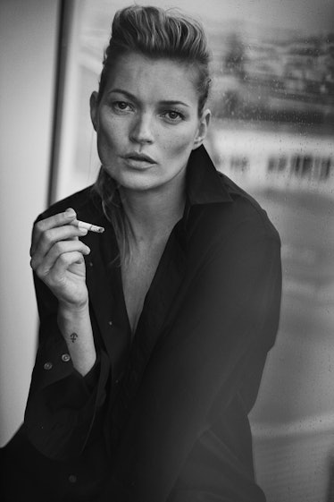 Kate Moss posing for a photo while wearing a black shirt and holding a cigarette