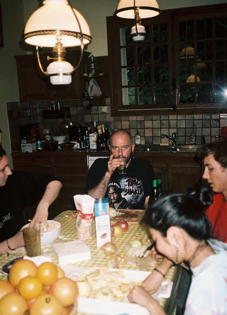 A model sitting at a dining tale with other models, having a drink in Vetements Summer Camp 